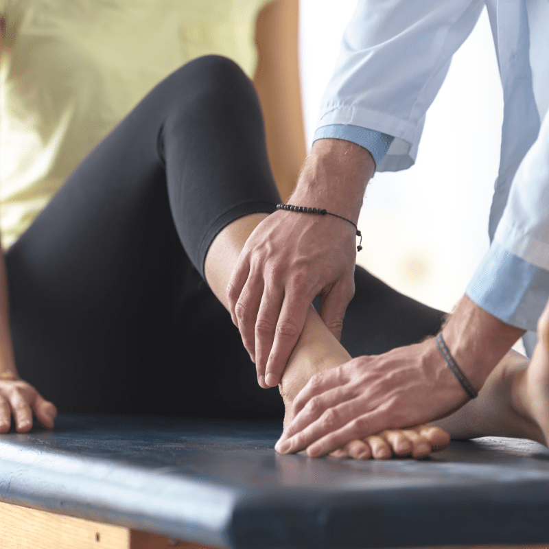 Patient sitting on exam table while physical therapist examines her injured ankle