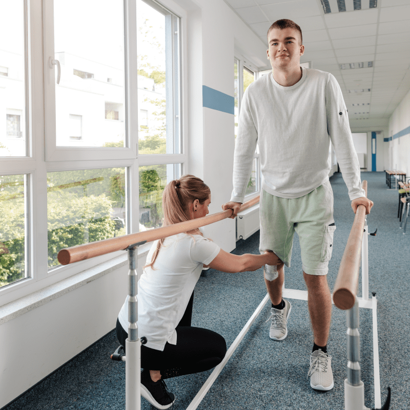 Physical therapist helping patient walk while holding hand rails