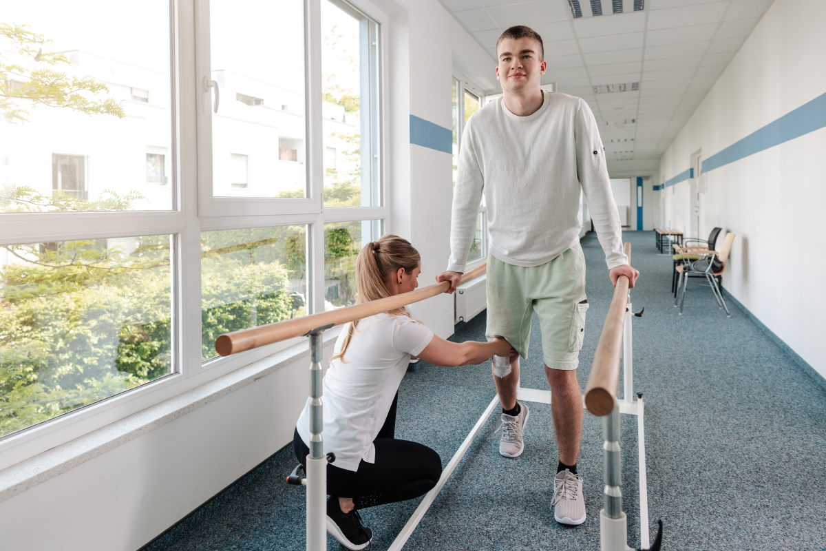 Physical therapist helping patient walk while holding hand rails