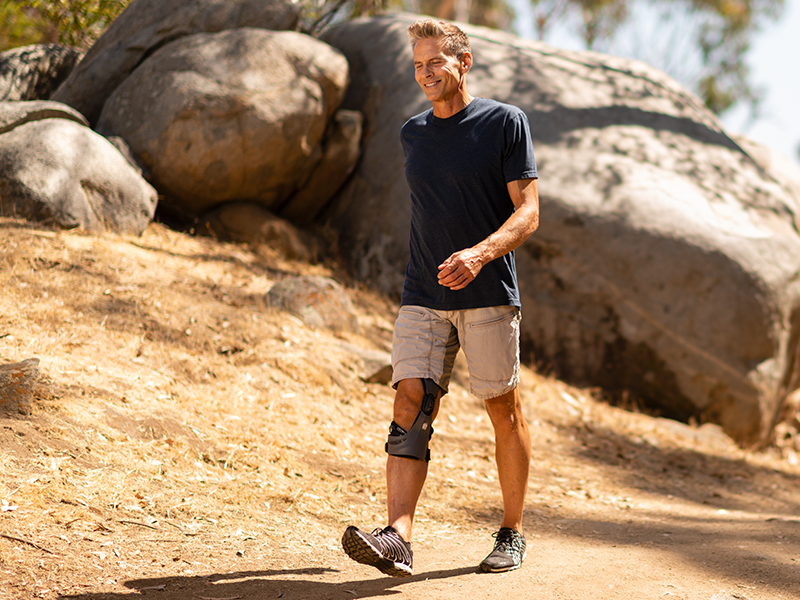 Man walking on a trail outside while wearing a knee brace