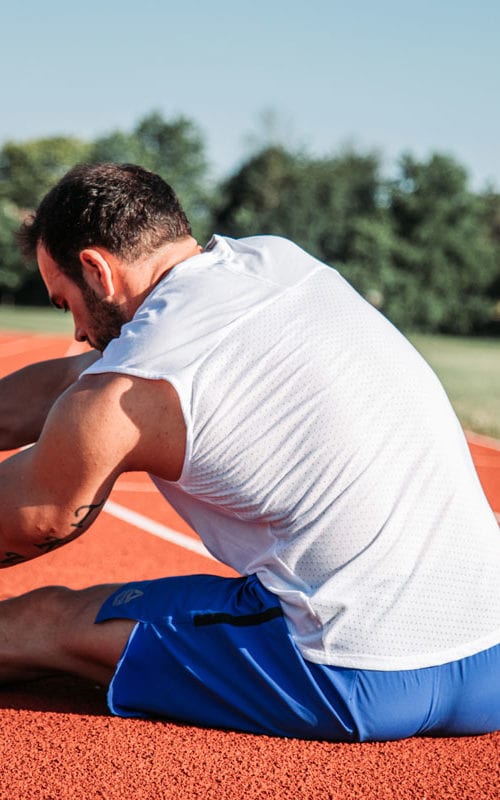 Athletic man sitting to stretch on track