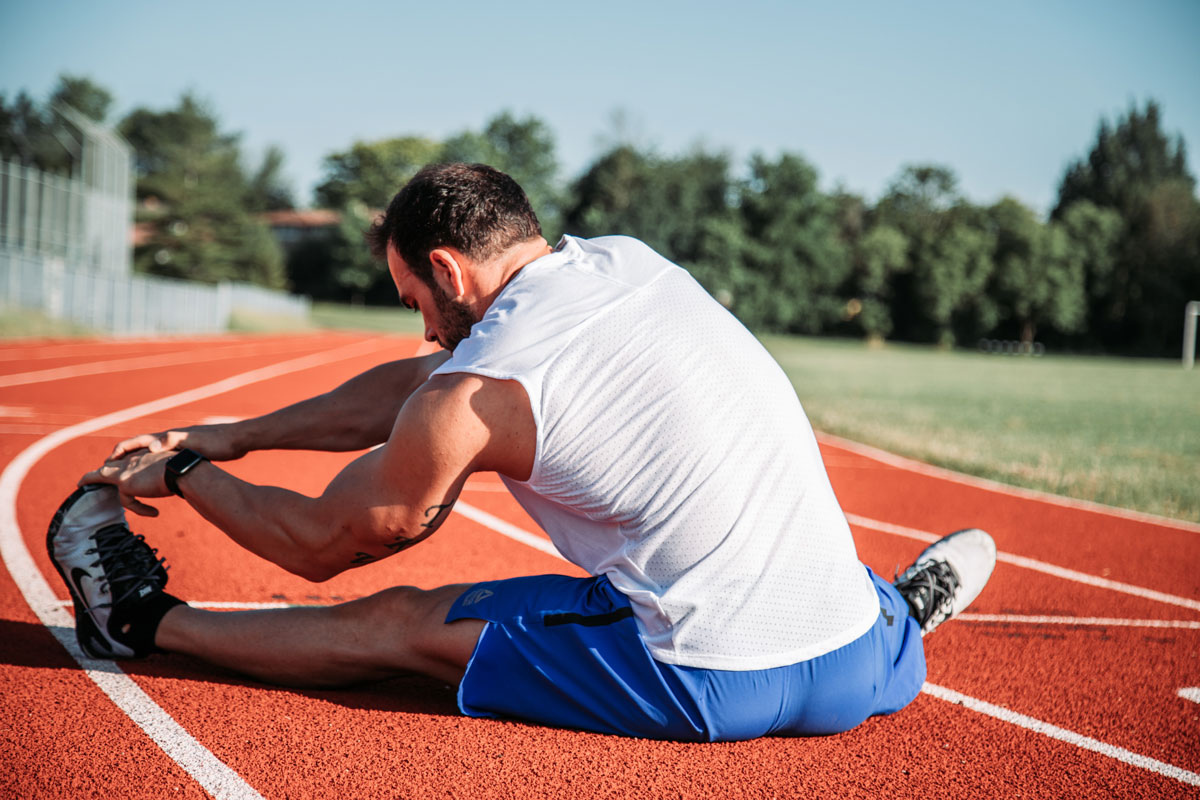 Athletic man sitting to stretch on track